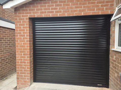 Black roller garage door fitted to a brick garage